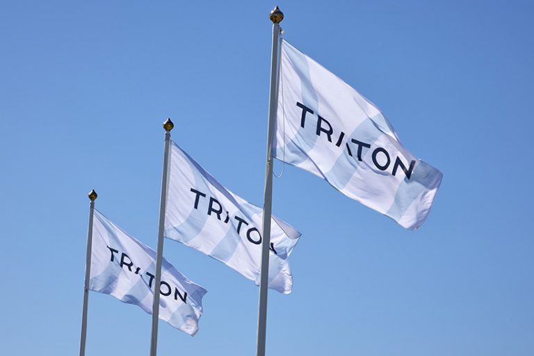 Das Bild zeigt Flaggen des Nutzfahrzeugherstellers Traton Group, die vor einem blauen Himmel im Wind wehen.