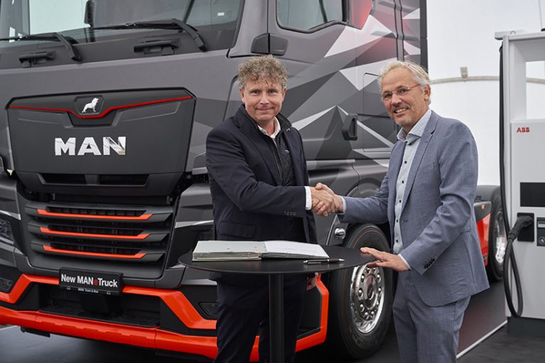 MAN Truck & Bus und ABB E-mobility verstehen sich: Im Vordergrund schütteln sich zwei Männer aus den beiden Unternehmen die Hände, im Hintergrund stehen links ein schwarzer MAN-Truck und rechts eine weiße ABB-Ladesäule.