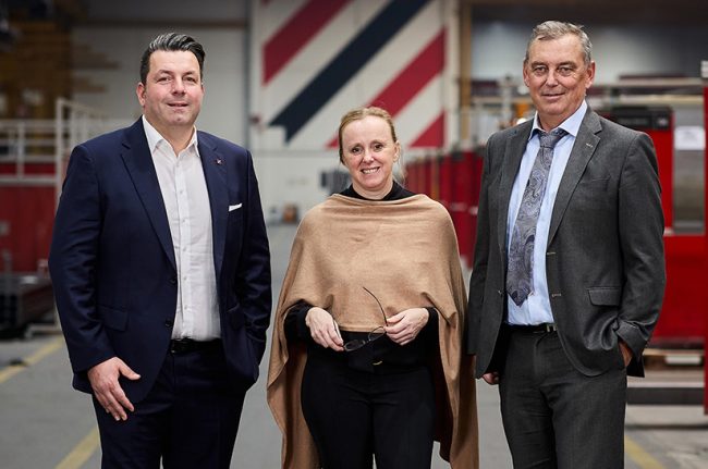Das Bild zeigt drei weiße Menschen in einer Werkshalle (v.l.n.r.): CSO Maik Spindler, CFO Daniela Lorenzer und COO Thomas Biringer. Gemeinsam bilden die drei die Geschäftsführung der Schwarzmüller Gruppe.