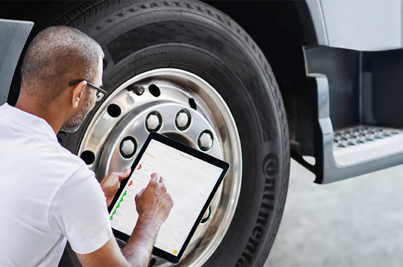 Digitales Reigenmanagement: Das Bild zeigt, wie ein Mann vor einem LKW-Reifen kniet und mit einem Tablet den Reifenzustand mittels der Software ContiConnect von Continental prüft.