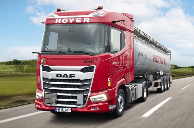 Zu sehen ist ein LKW mit einer roten Zugmaschine während der Fahrt. Es handelt sich dabei um einen neuen DAF XG 480 von Hoyer.