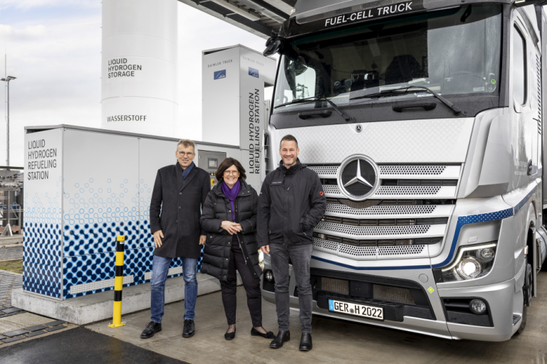 Die sLH2-Technologie bringt Linde und Daimler Truck zusammen, die zusammen die erste öffentliche Tankstelle betreiben. Das Bild zeigt diese Tankstelle ebenso wie einen silbernen Truck mit Stern und drei Menschen, die vor diesem Fahrzeug stehen.