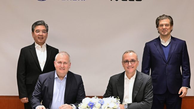 Hyundai liefert vollelektrisches leichtes Nutzfahrzeug an Iveco in Europa. Das Bild zeigt das Führungspersonal beider Häuser bei der feierlichen Unterschrift. Zwei Männer sitzen an einem Tisch, vor sich die Vertragsunterlagen und zwischen ihnen ein Strauß Blumen. Hinter ihnen stehen zwei weitere Männer.