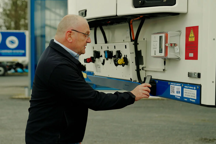 Krone_Smart_Assistant_web Das Bild zeigt einen Mann, der hinter einem LKW steht und mit seinem Smartphone einen QR-Code scannt. Er nutzt eine neue Lösung von Krone.