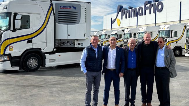 Das Bild zeigt im Vordergrund fünf Männer,das Führungspersonal von Schmitz Cargobull und Primafrio, und im Hintergrund , mehrere LKW sowie eine Werkshalle.