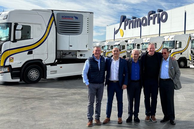 Das Bild zeigt im Vordergrund fünf Männer,das Führungspersonal von Schmitz Cargobull und Primafrio, und im Hintergrund , mehrere LKW sowie eine Werkshalle.