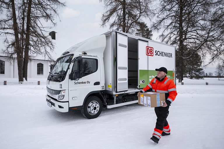 Das Bild zeigt einen Fuso Canter im Schnee. Vor dem Fahrzeug läuft ein Mitarbeiter mit einem Paket.