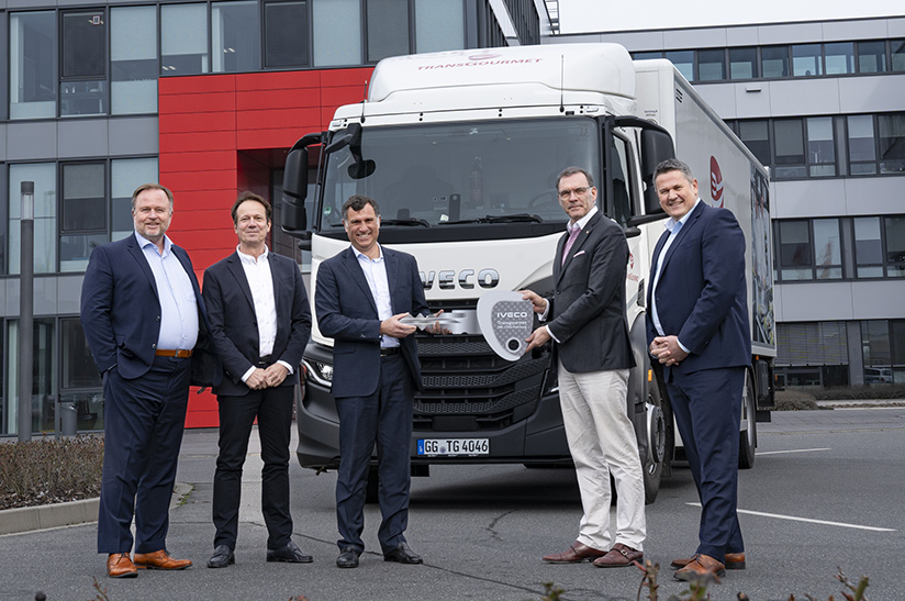 IVECO_Transgourmet_200_CNG_1 (web) Das Bild zeigt fünf Männer vor einem Iveco-LKW, der von Transgourmet Deutschland betrieben wird. Zwei der Männer halten einen überdimensionalen Schlüssel in der Hand.
