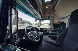 Das Bild zeigt die Kabine des neuen Mercedes-Benz Actros 600 L von Daimler Truck. Die Perspektive ist bei geöffneter Fahrertür leicht schräg auf das Lenkrad.