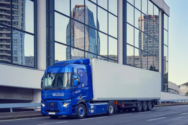 Das Bild zeigt einen blauen LKW von Renault Trucks. Hinter dem LKW ist eine spiegelnde Fassade zu sehen.