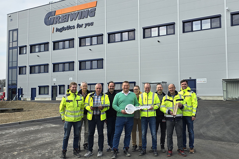 Das Bild zeigt Mitarbeiter des Logistikunternehmens Greiwing mit einem überdimensionalem Schlüssel Im Hintergrund ist das neu eröffnete Logistikzentrum zu sehen.