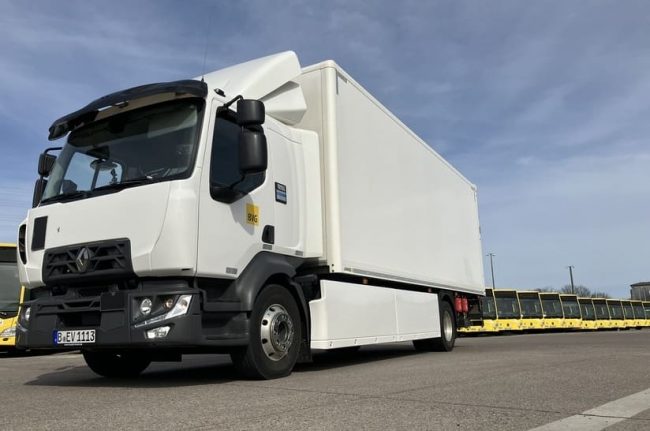Das Bild zeigt im Vordergrund einen weißen Renault Trucks E-Tech D. Im Hintergrund sind gelbe Busse der Berliner Verkehrsbetriebe zu sehen.