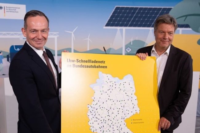 Zwei Bundesminister halten eine Karte für das Lkw-Schnellladenetz hoch.