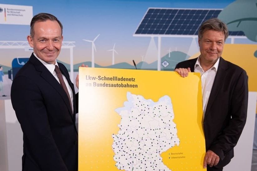 Zwei Bundesminister halten eine Karte für das Lkw-Schnellladenetz hoch.