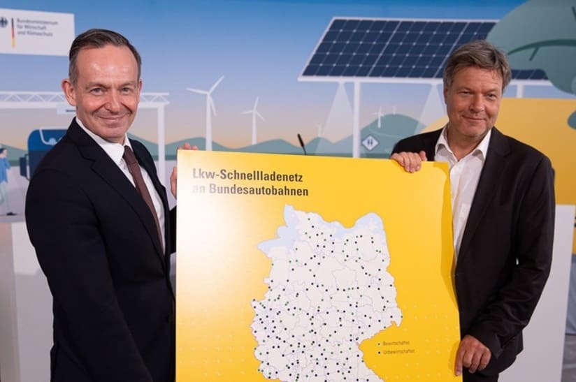 Zwei Bundesminister halten eine Karte für das Lkw-Schnellladenetz hoch.